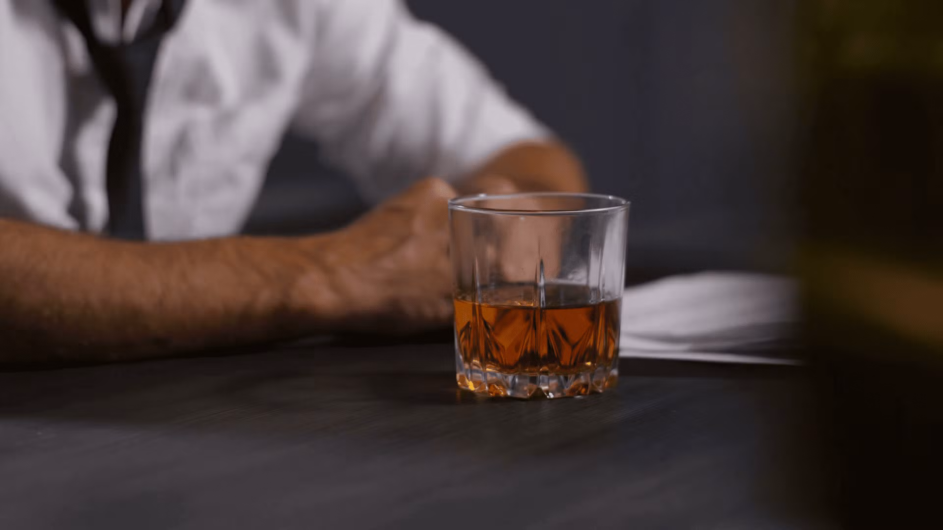 videoblocks-close-up-of-male-hand-holding-glass-of-whiskey-against-office-desk-with-bottle-and-documents-background-depressed-businessman-relieving-emotional-stress-and-drinking-whiskey-at-office-dolly-shot-suvhvn-1.png